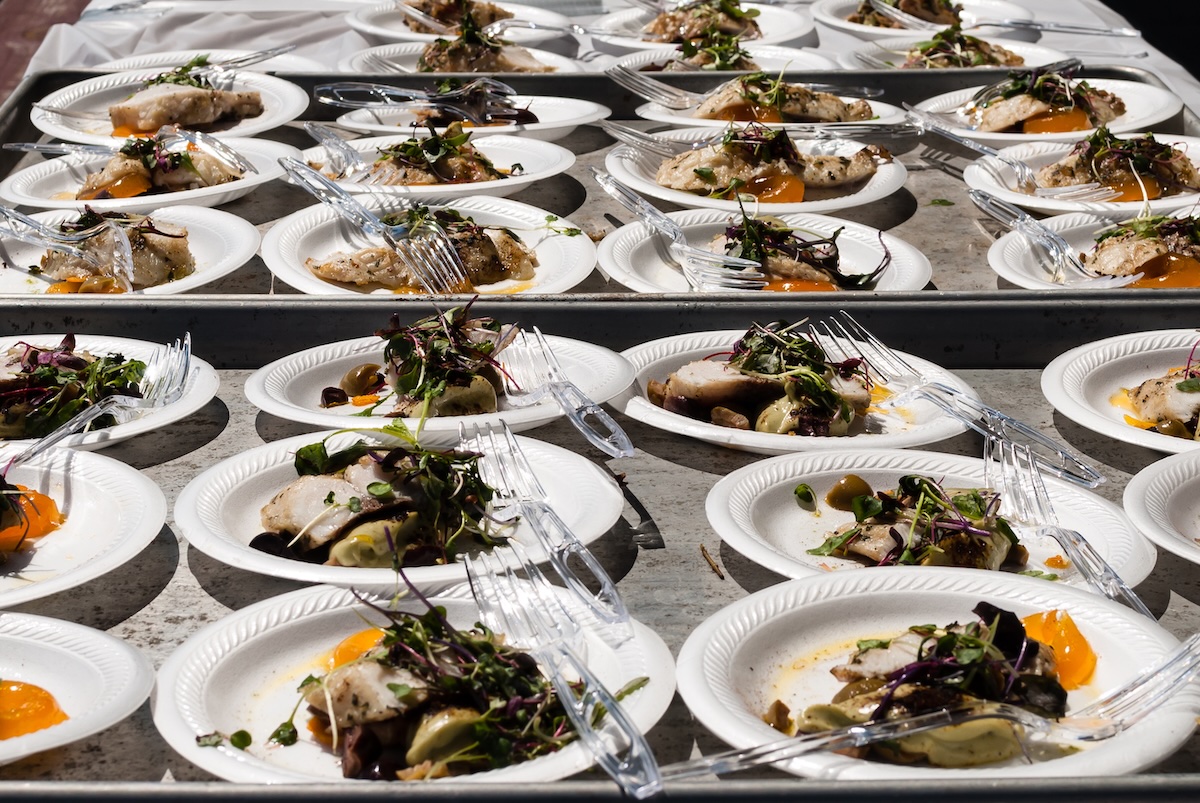 More than a dozen plates of blue catfish fillets with salad rest on a metal table.