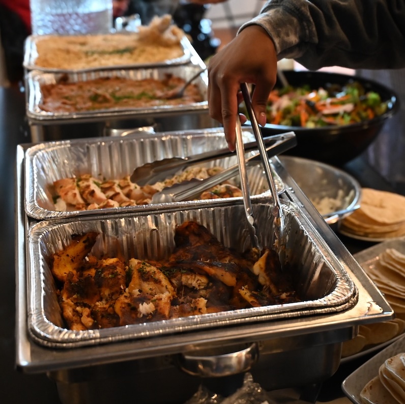 A hand with tongs reaches for blue catfish in a buffet dish.